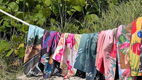 Collection de serviettes de plage Kawelä en microfibre suspendues sur corde à linge, designs tropicaux colorés variés