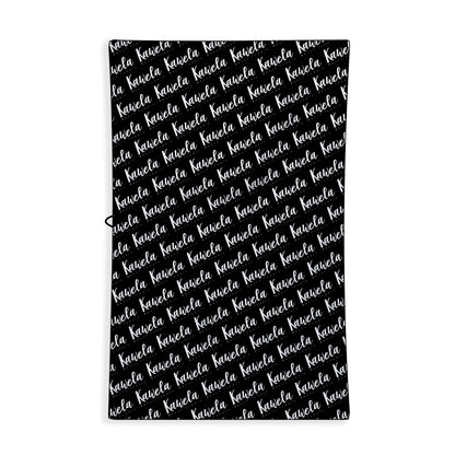 Serviettes de plage noires Kawelä FREEPORT, tissu doux et absorbant, pliées sur une surface en bois.