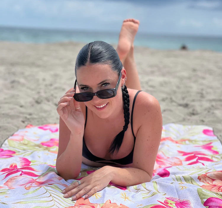 Femme relaxant sur serviette de plage Kawelä en microfibre avec motifs floraux tropicaux roses, lunettes de soleil
