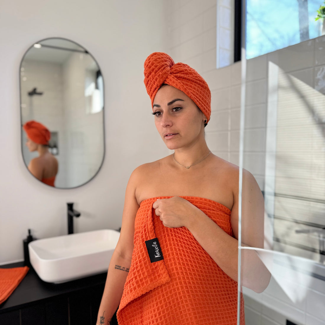 Serviette de bain orange KAWELÄ NARANJA avec texture douce, pliée sur une surface blanche, idéale pour la salle de bain.
