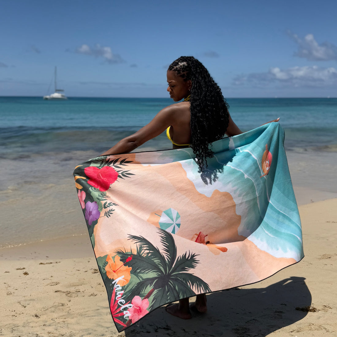 Serviette de plage KAWELÄ LE DIAMANT avec motif géométrique coloré sur sable.