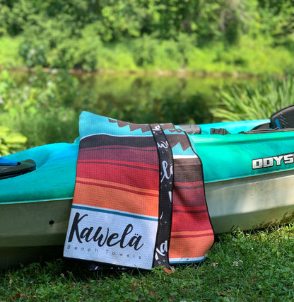 Serviette de plage KWATNA PEAK de la marque KAWELÄ avec motifs colorés, étendue sur le sable.